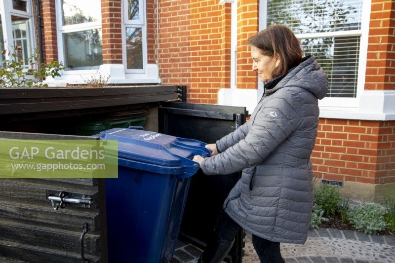 Garden owner, woman in her front garden placing wheely bin into garden store
