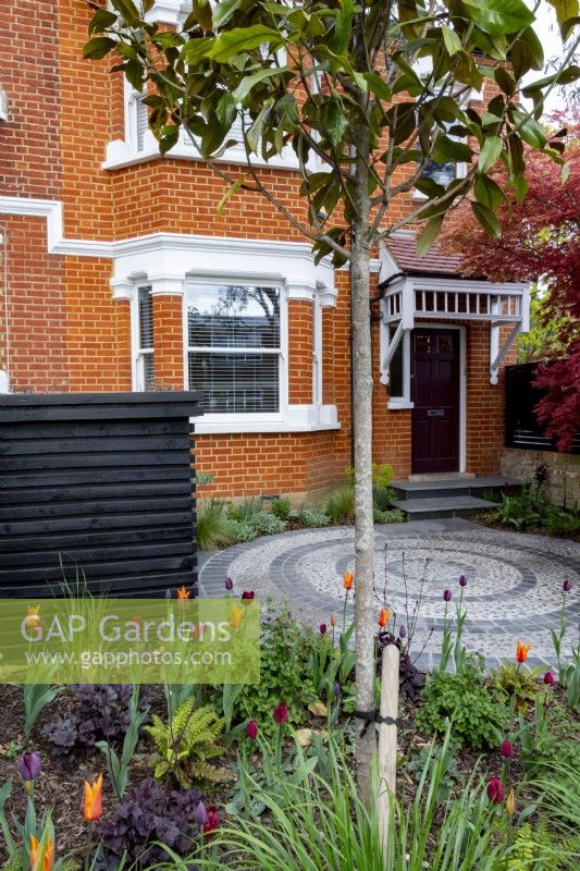Small suburban front garden in April with bin store and spring borders

