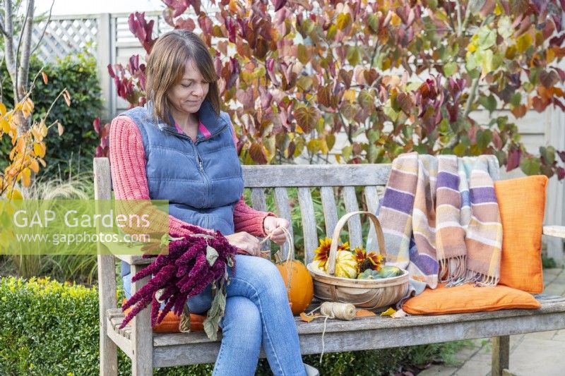 Woman sitting on bench tying together Amaranthus flowers