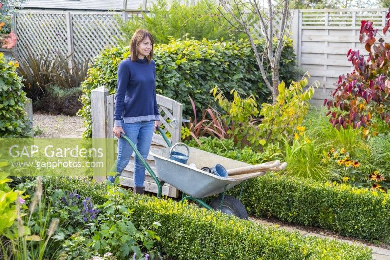 Woman pushing wheelbarrow through garden