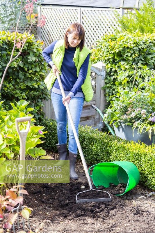 Woman using rake to spread compost over bed