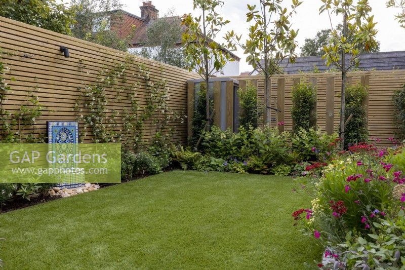 Contemporary suburban garden in London with colourful borders  and artificial lawn