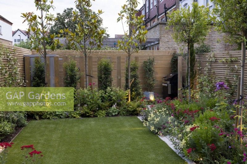 Contemporary suburban garden in London with colourful borders, artificial lawn and lighting