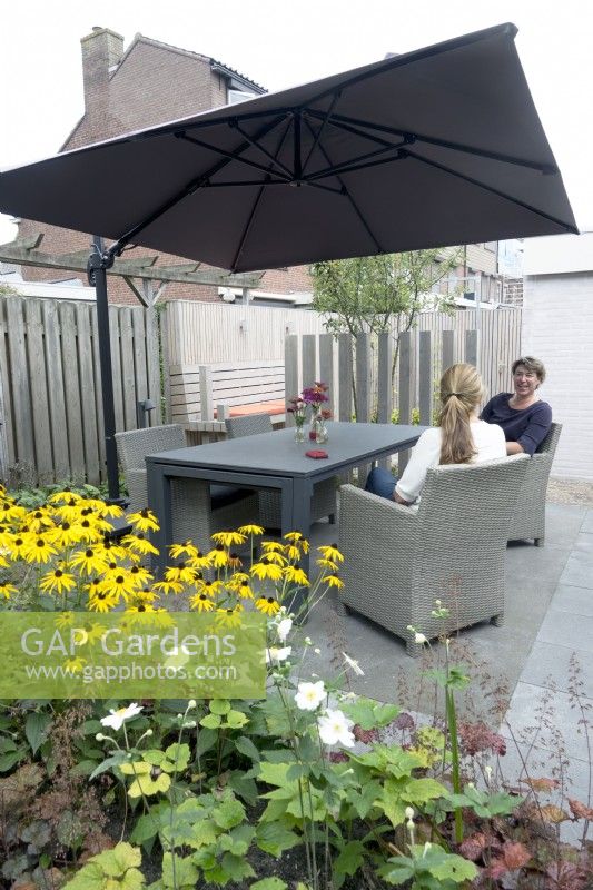 Women sat by modern table in small urban garden with Rudbeckia in foreground.