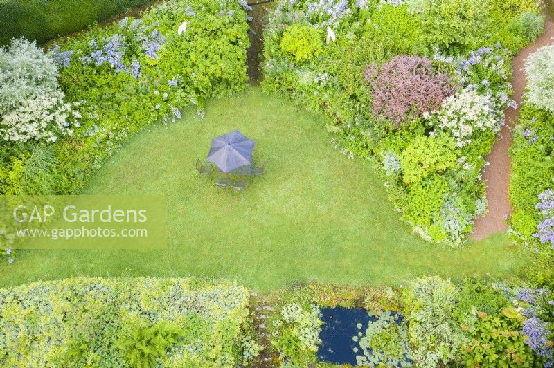 View over lawn and borders with parasol and chairs on lawn; image taken with drone. July. Summer.