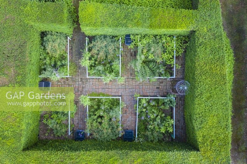 View over small formal garden contained by clipped Yew hedges; image taken with drone. Brick paths and rectangular beds contained by railings July. Summer.