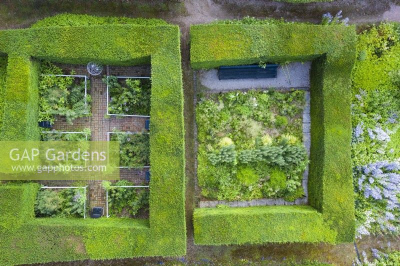View over two small formal gardens contained by clipped Yew hedges; image taken with drone. Brick paths and rectangular beds contained by railings; image taken with drone. July. Summer.