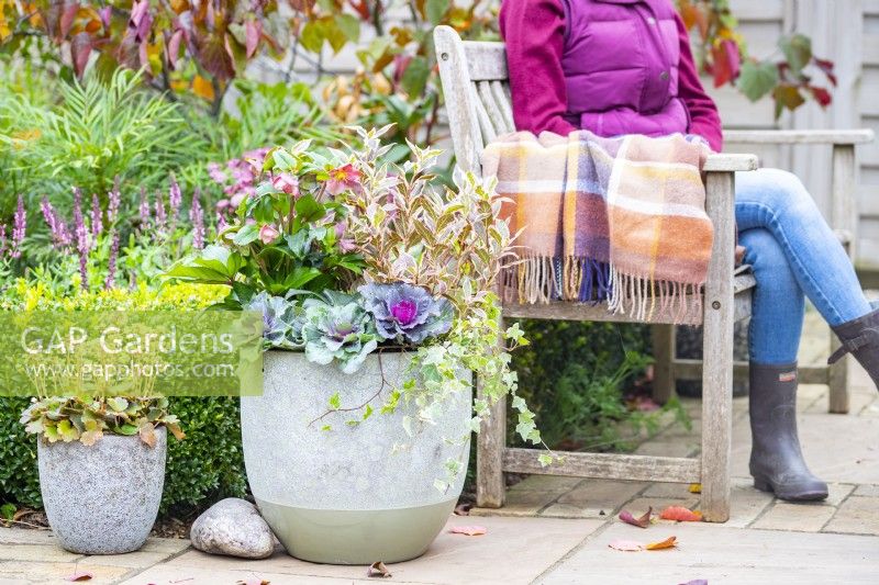 Person sitting on a wooden bench next to Autumn container arrangement