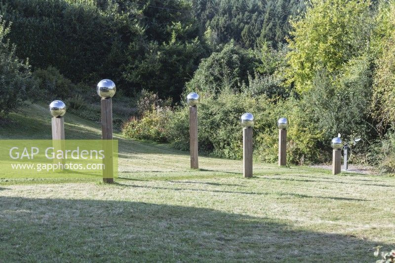 Avenue in mown meadow of stainless steel globes mounted on wooden posts. October, Autumn. 