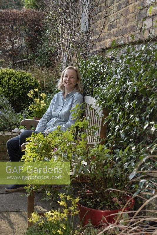 Woman sitting at the garden table surrounded by Narcissus 'Hawera', Trachelospermum jasminoides.
