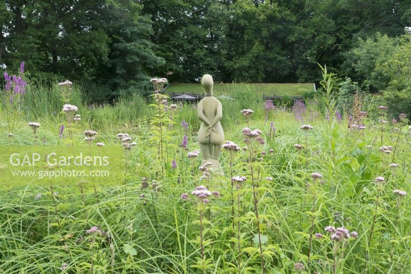 Sculpture of woman standing in between grasses on the edge of pond.