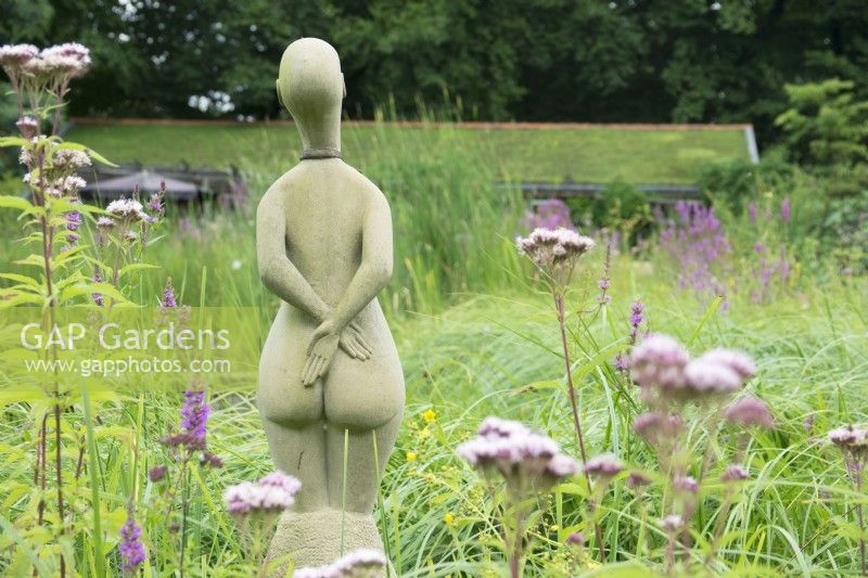 Sculpture of woman standing in between grasses on the edge of pond.
