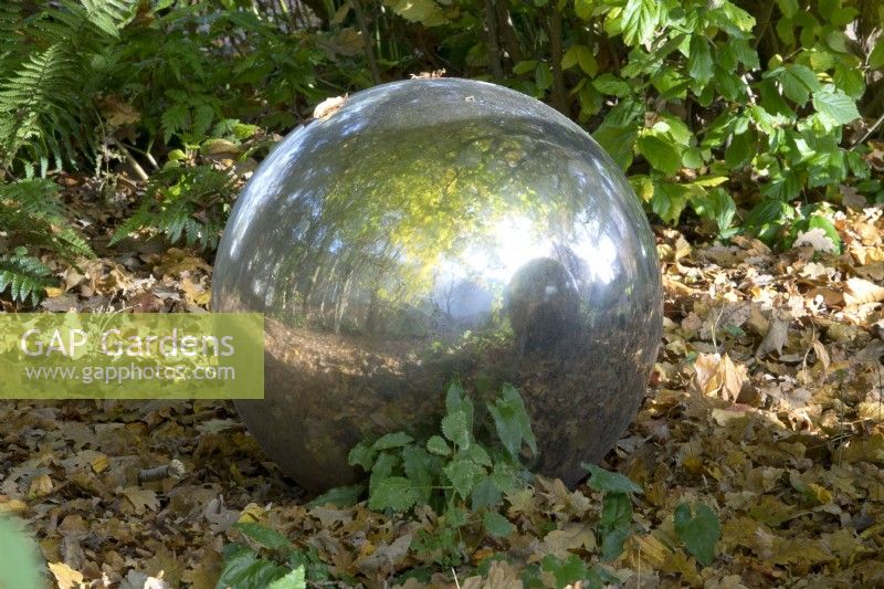 Large mirror ball laying in autumn leaves reflecting the garden.