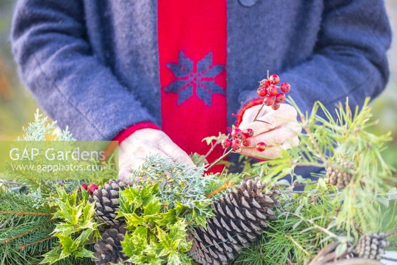 Woman adding red berries to the wreath