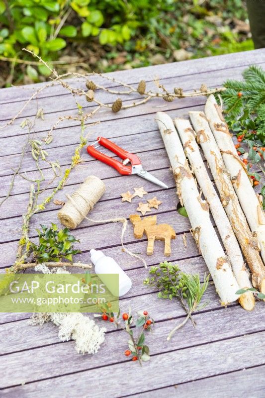 Birch sticks, various foliage, bark stars, wooden reindeer, string, glue and snips laid out on table