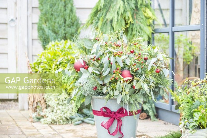 Christmas container arrangement with Eucalyptus, Hypericum, Pinus and Thuja decorated with a ribbon bow and baubles