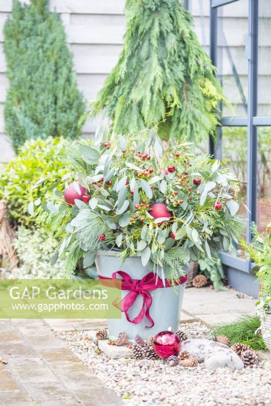 Christmas container arrangement with Eucalyptus, Hypericum, Pinus and Thuja decorated with a ribbon bow and baubles