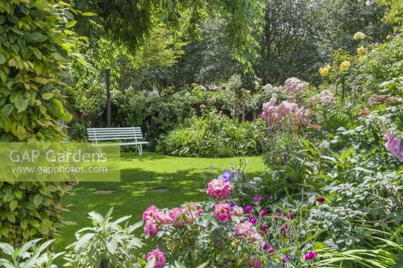 View of garden with painted wood seat, informal lawn and mixed borders - June