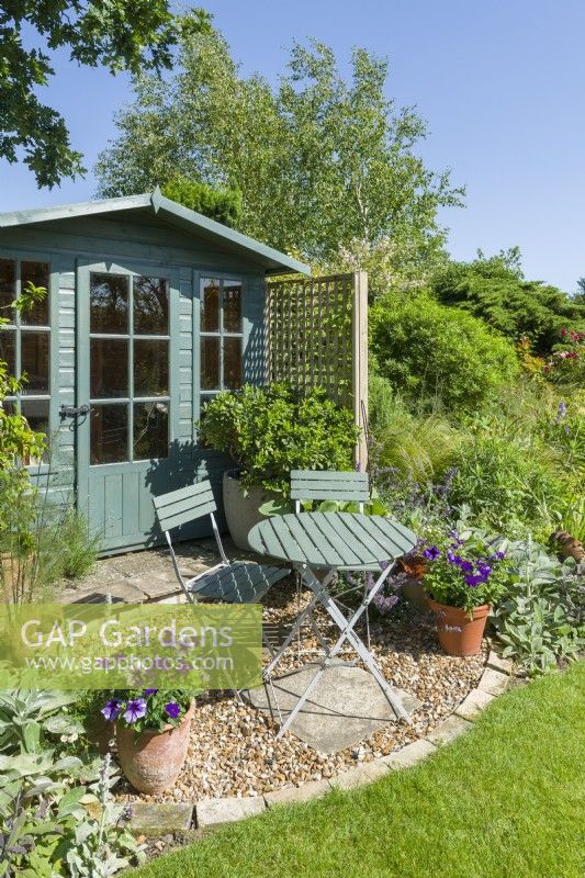 Summer house with table and chairs. Petunias in pots. June