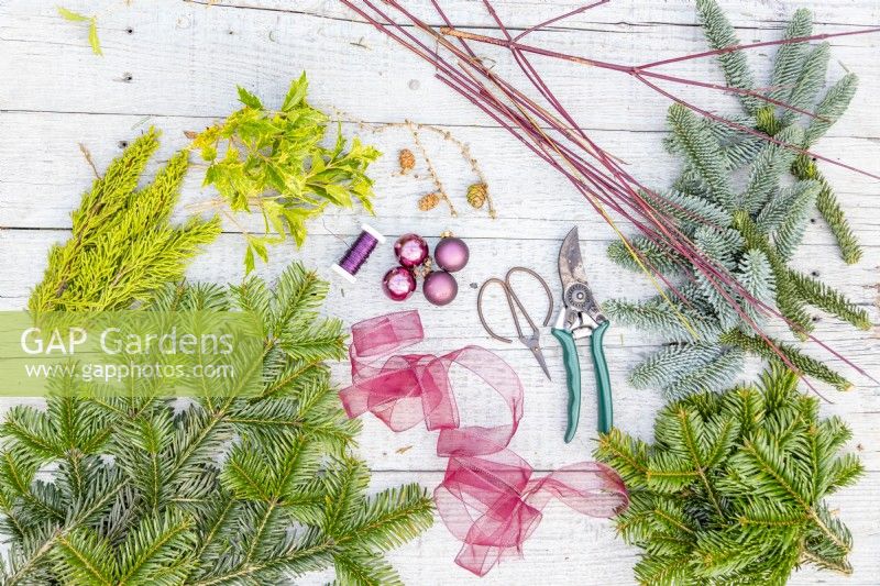 Evergreen foliage, dogwood twigs, ribbon, pine cones, baubles, wire, pruning scissors and secateurs laid out on a wooden surface