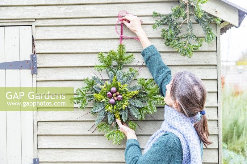 Woman hanging Evergreen star on a pale green wooden wall