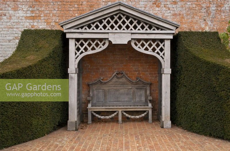 An ornate carved wood gazebo and garden bench outside the walled garden at Thenford Gardens and Arboretum, Thenford, Burford, Oxfordshire, UK