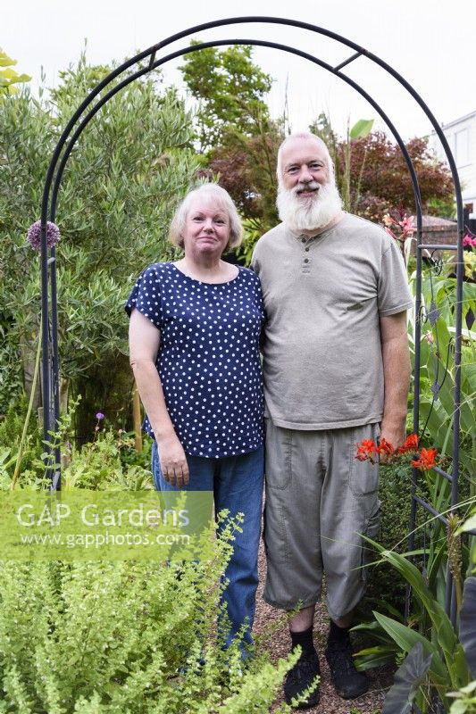 Couple standing under arch in their garden in August.