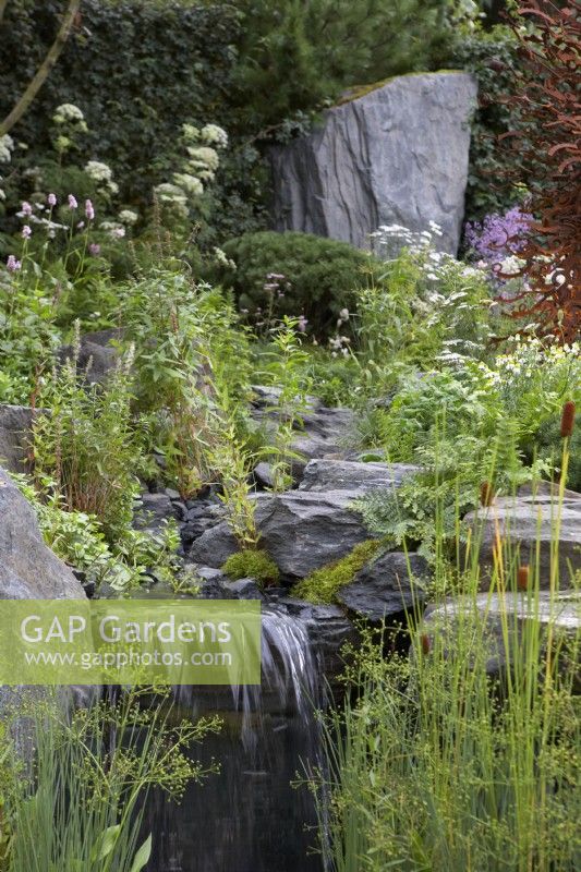 Bodmin Jail: 60 Degrees East - A Garden Between Continents. Designers: Ekaterina Zasukhina and Carly Kershaw. Waterfall, rocks and naturalistic planting. Chelsea Flower Show 2021.