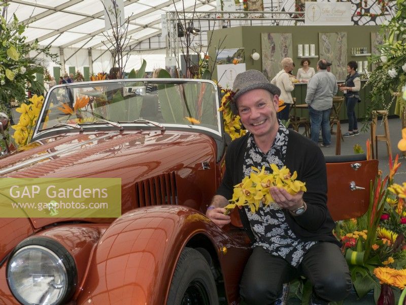 Jonathan Moseley the floral designer next to a Morgan car in Malvern and holding a yellow display of Orchid flowers.