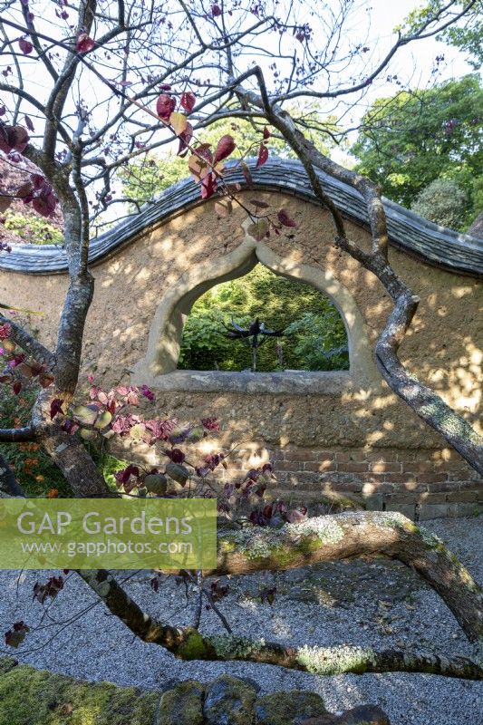 Cob wall structure in garden, with 'wavy' top and arched window 'peephole'