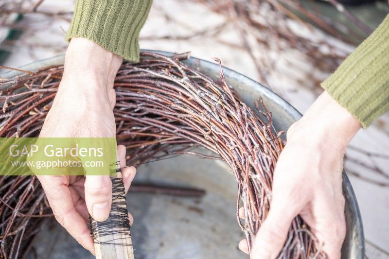 Woman wrapping wire around the birch sticks to form the homemade wreath