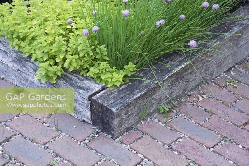 Detail of raised bed with herbs and red brick gravel path 