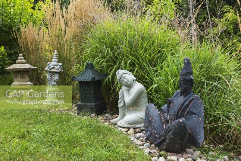 Asian sculptures and Chinese lanterns in rock border in backyard garden in summer, Quebec, Canada - August