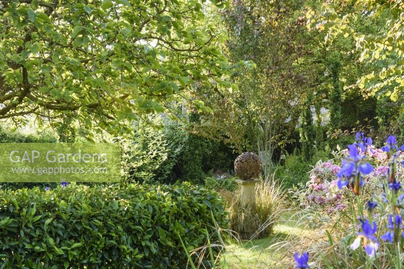 Country garden in June with a decorative metal sphere surrounded by lush planting.