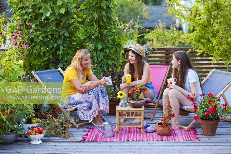 Women relaxing on roof terrace, container plants include tomatoes, herbs and flowers.