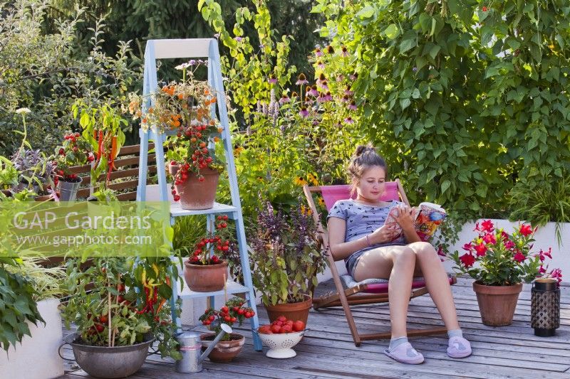 Girl relaxing on roof terrace with raised bed and container grown vegetables and herbs.
