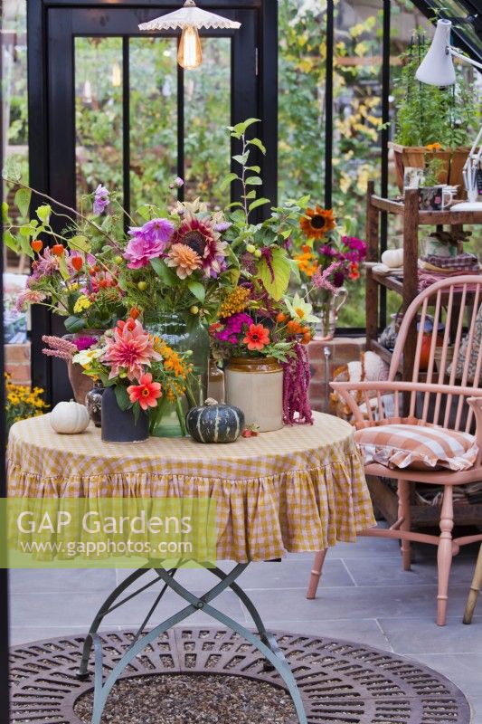 Floral arrangement with vases and cut flowers including Dahlias, Amaranthus, Hellianthus, Zinnia, Physalis, Cosmos and pumpkins on the table.