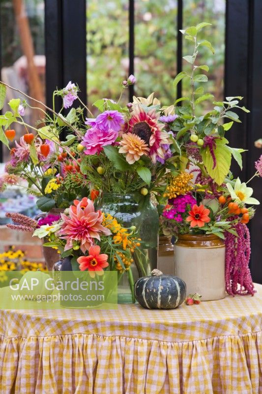 Floral arrangement with vases and cut flowers including Dahlias, Amaranthus, Hellianthus, Zinnia, Physalis, Cosmos and pumpkins on the table.