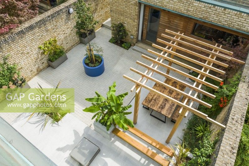 Aerial view of a contemporary courtyard garden with pergola, outdoor seating, large planters and plants with a tropical appearance. September