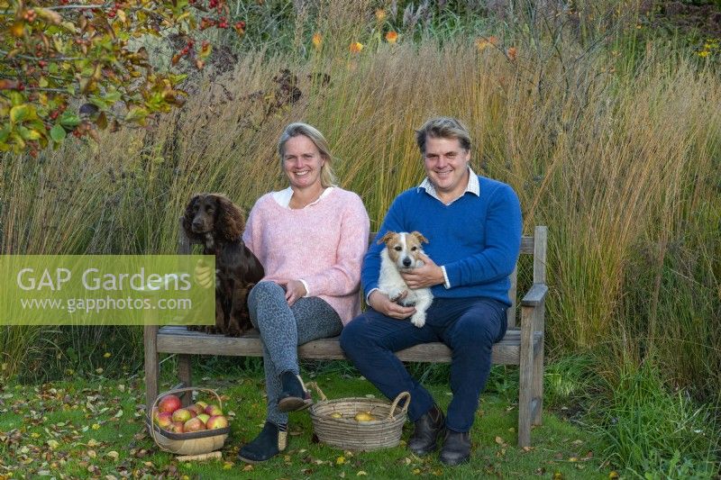 Couple sitting on bench with pet dogs after harvesting apples.
