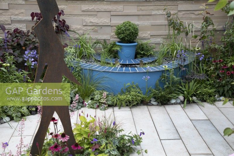 'The Lillian Prime Trust Garden' - BBC Gardener's World Live 2021 - semi circular pond painted blue, bordered by perennials in pastel shades, with hands sticking out of the water