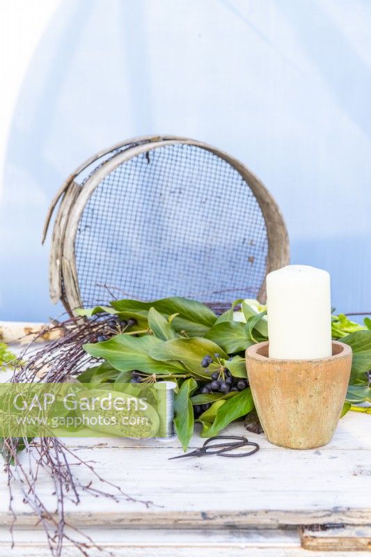 Candle, pot, gardening scissors, wire, gravel, sieve, birch sticks and Ivy laid out on a wooden surface