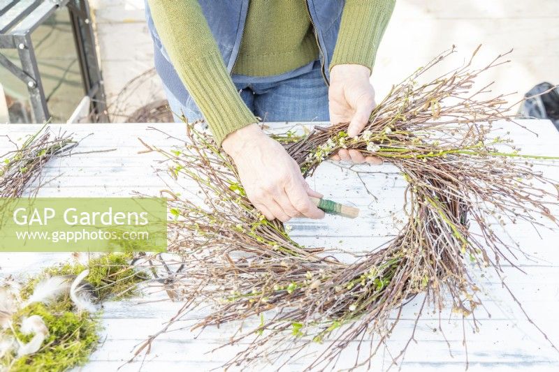 Woman wiring the bundles of twigs and seed heads to the wreath
