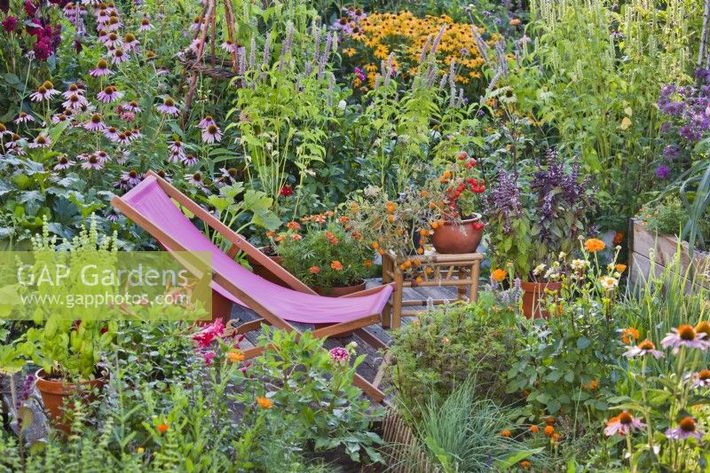 Deckchair on smal patio amongst colourful mixed border and containers.