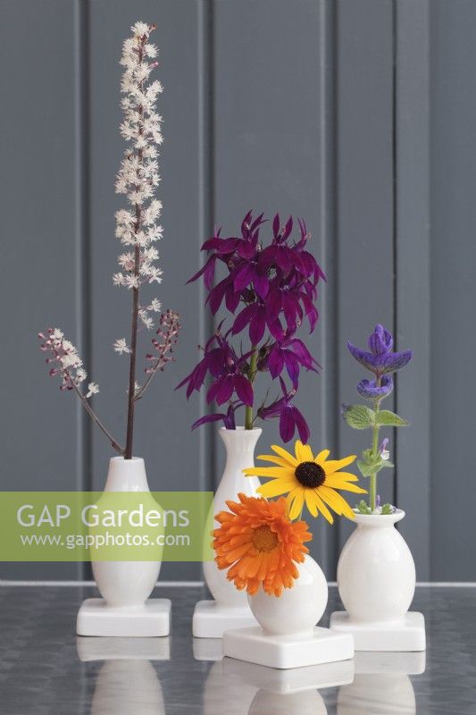 Colourful late summer flowers in bud vases against grey wooden wall - September