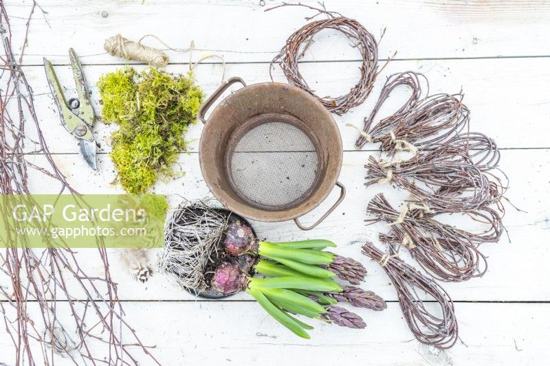 Sieve, moss, secateurs, string, feathers, birch twig loops and hyacinths laid out on a wooden surface