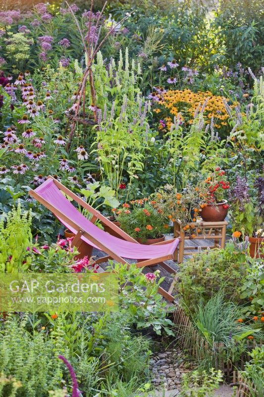 Deckchair on small patio amongst colourful mixed border and containers.