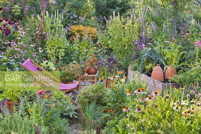 Deckchair on small patio amongst colourful mixed border, raised vegetable bed and herb bed.