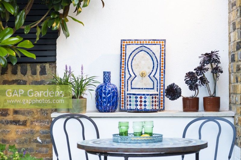 Mediterranean style corner with a table, chairs and moroccan tile fountain in small urban garden. 