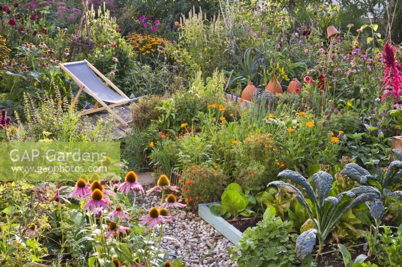 Organic kitchen garden with raised beds and small patio with a deckchair.
